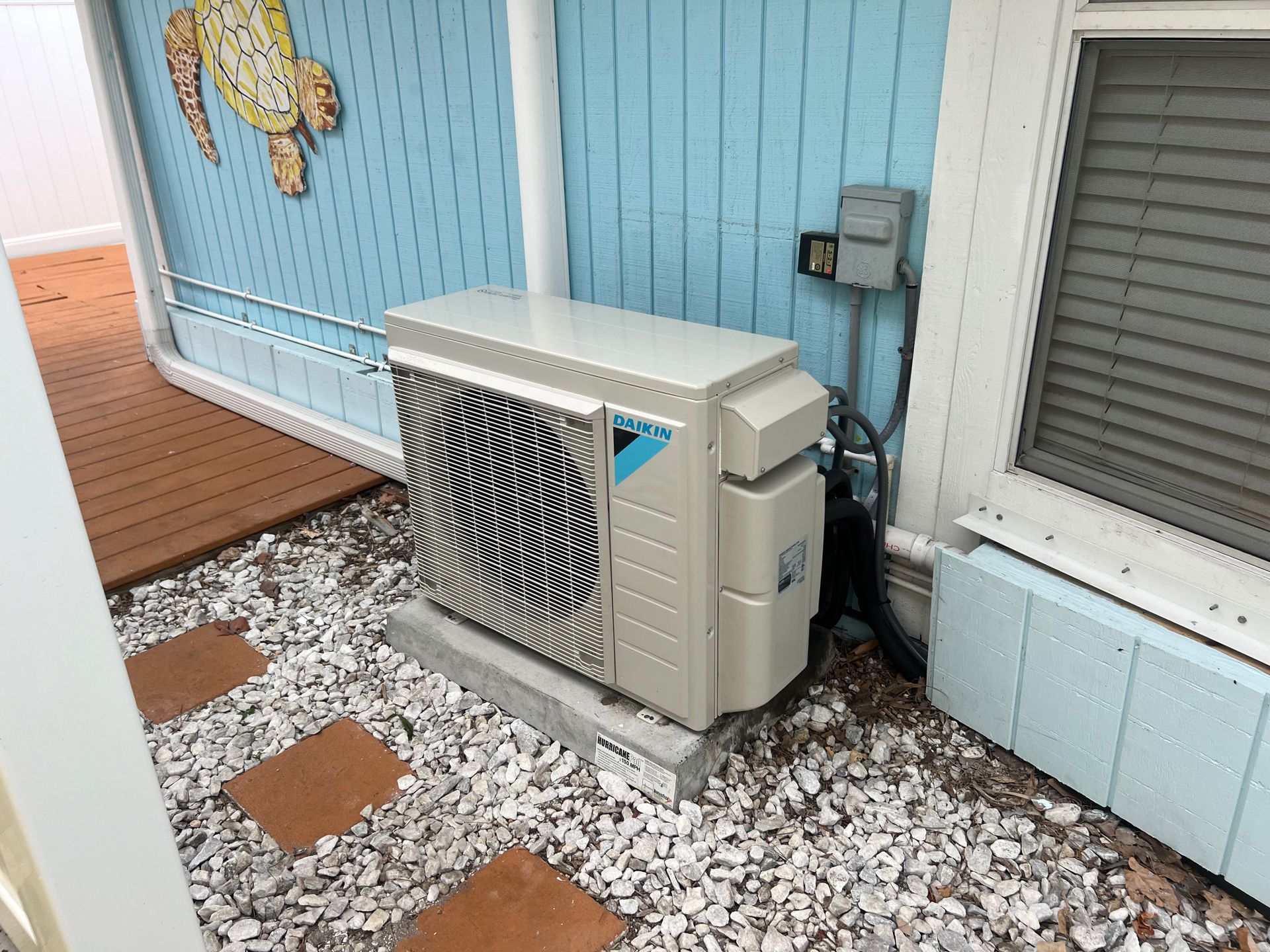 Outdoor air conditioning unit next to a light blue wall and a window.