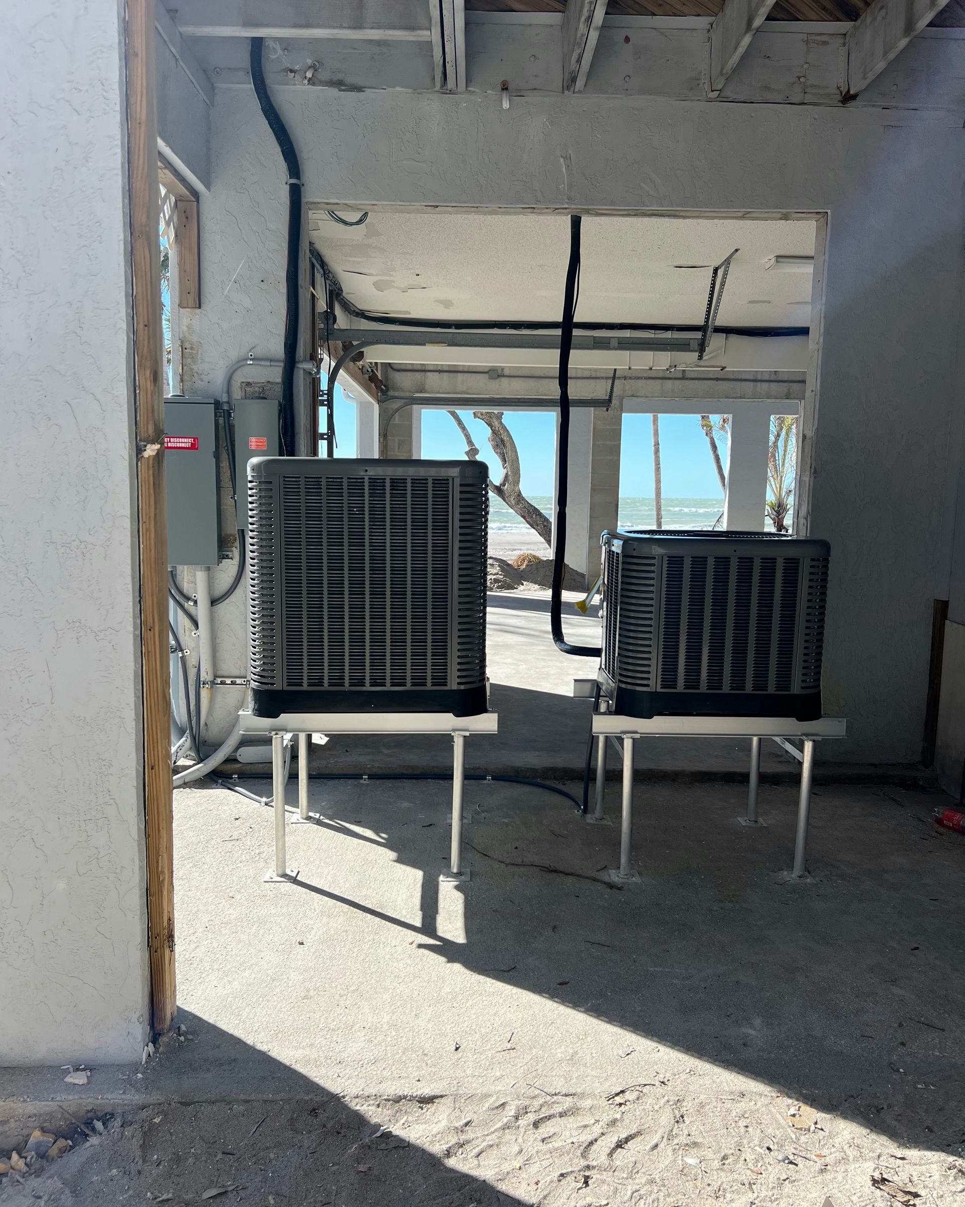 Two large, gray evaporative coolers on metal stands in an open-air building, sunlight streaming in.
