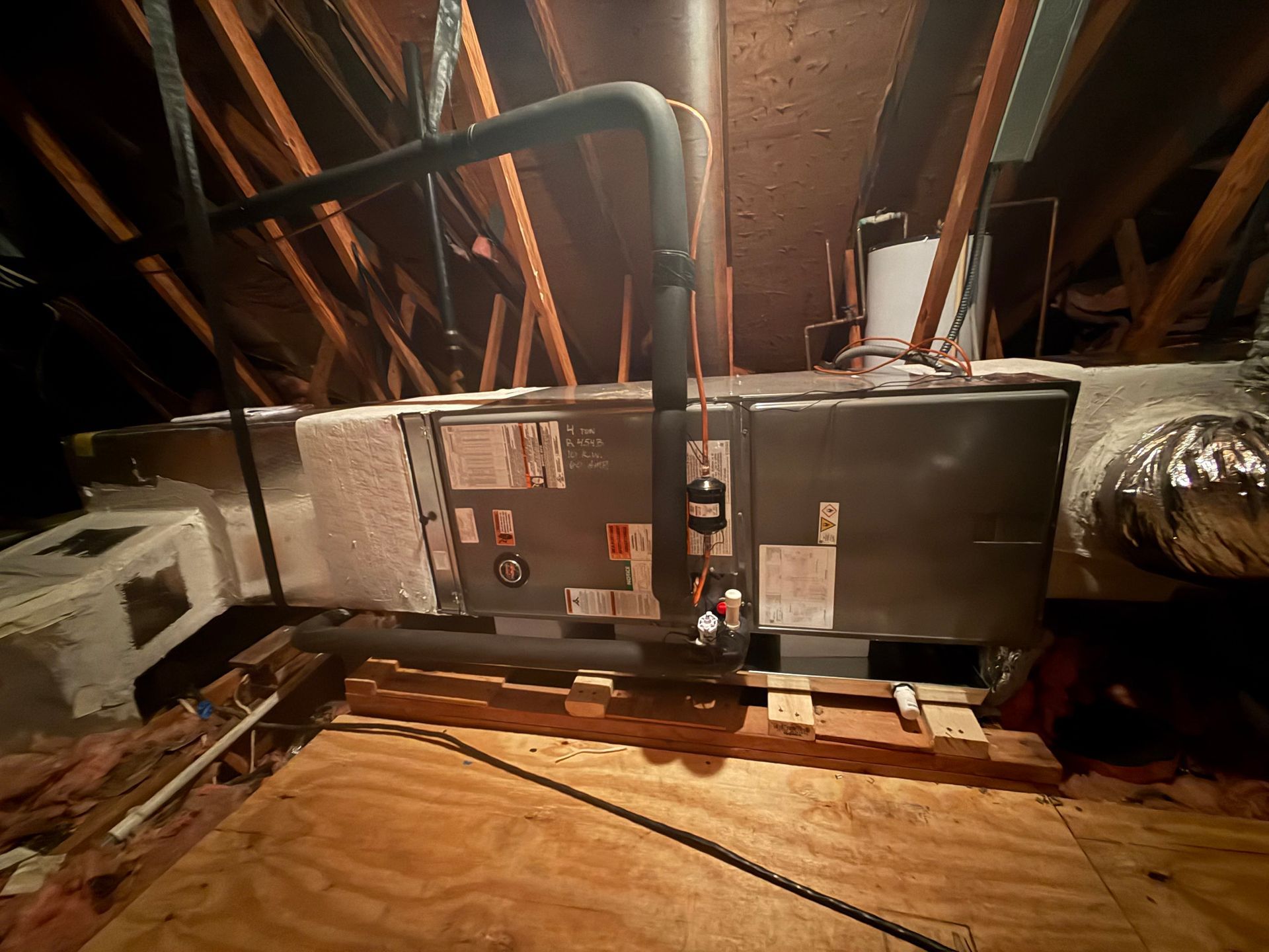 HVAC unit in an attic with ductwork, wooden beams, and insulation.