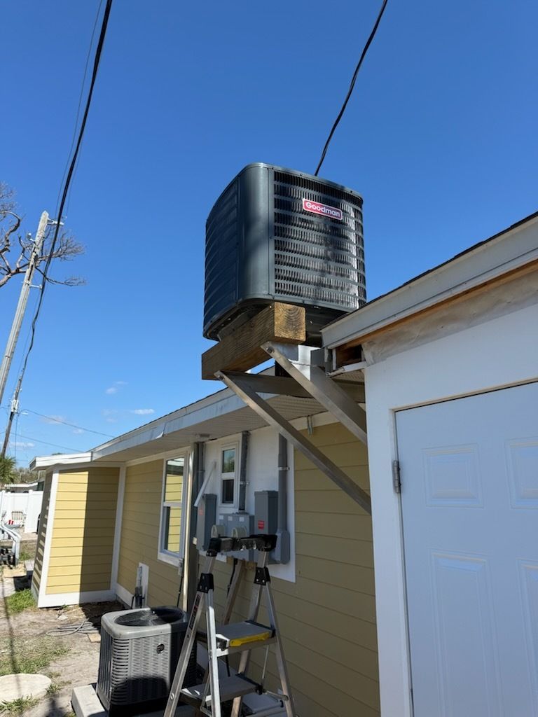 Black rooftop water heater on a house beside a white garage under a clear blue sky
