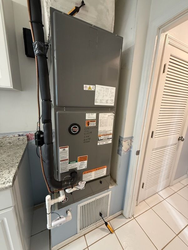 Gray HVAC furnace mounted in a utility closet with exposed ductwork and pipes