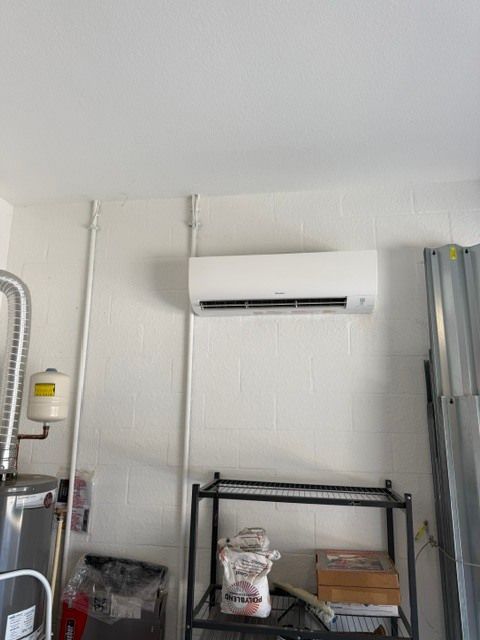 White wall with a mounted air conditioner above a metal shelving unit and cluttered storage items.