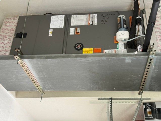 Ceiling-mounted HVAC unit with silver ductwork and metal support brackets in a utility space