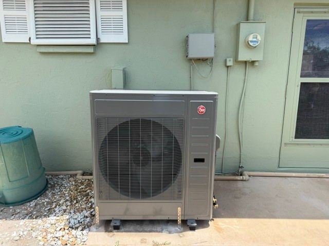 Outdoor HVAC unit beside a house wall and door, with utility boxes and gravel landscaping.