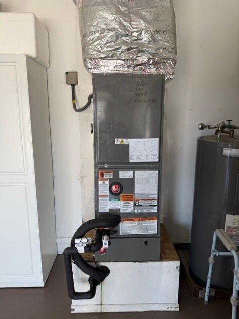 Gray HVAC furnace with ductwork and a black vent hose in a utility room beside a water heater