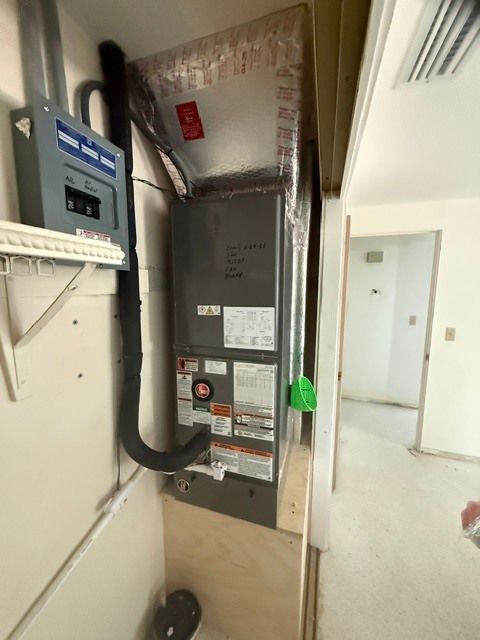 Electrical panel in utility closet with exposed ductwork, conduit, and a hallway visible to the right.