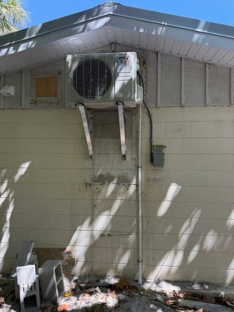Window AC unit mounted in a house wall with two support brackets and fallen debris below