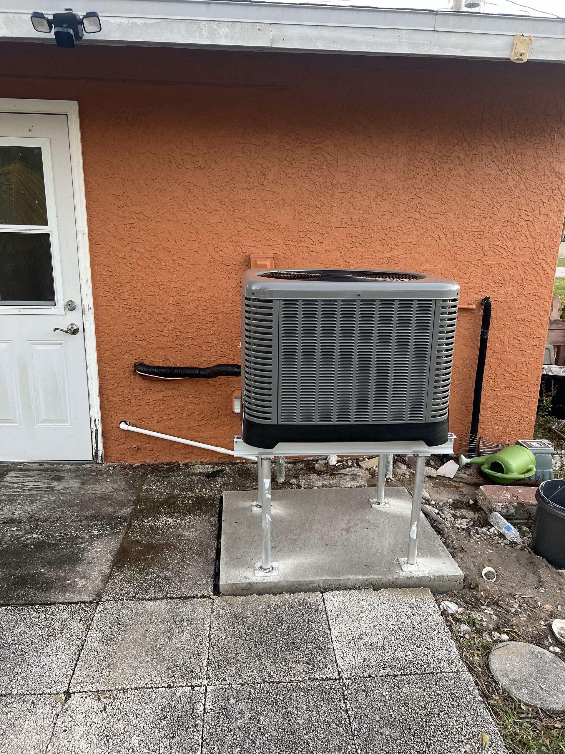Outdoor AC unit on a concrete pad, against an orange stucco wall, near a white door and stone patio.