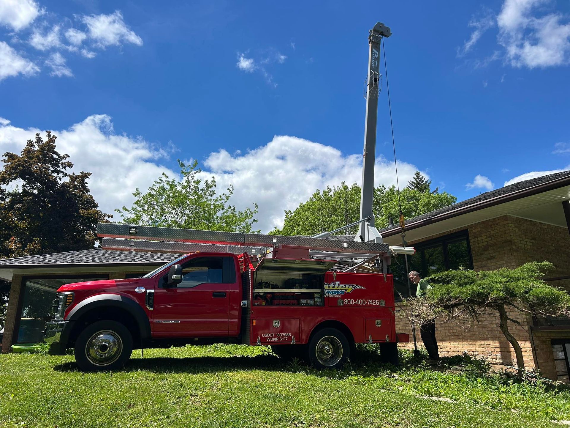Red utility truck parked beside a brick house under a blue sky with clouds