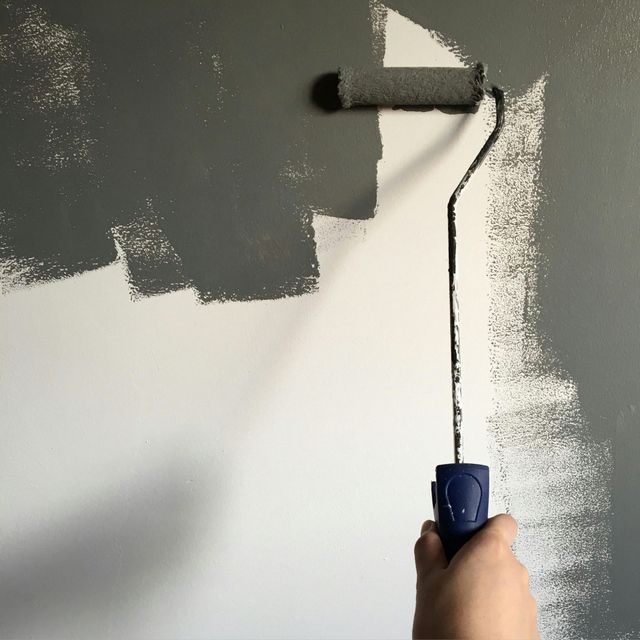 Hand painting a gray wall with a paint roller, showing progress from white.