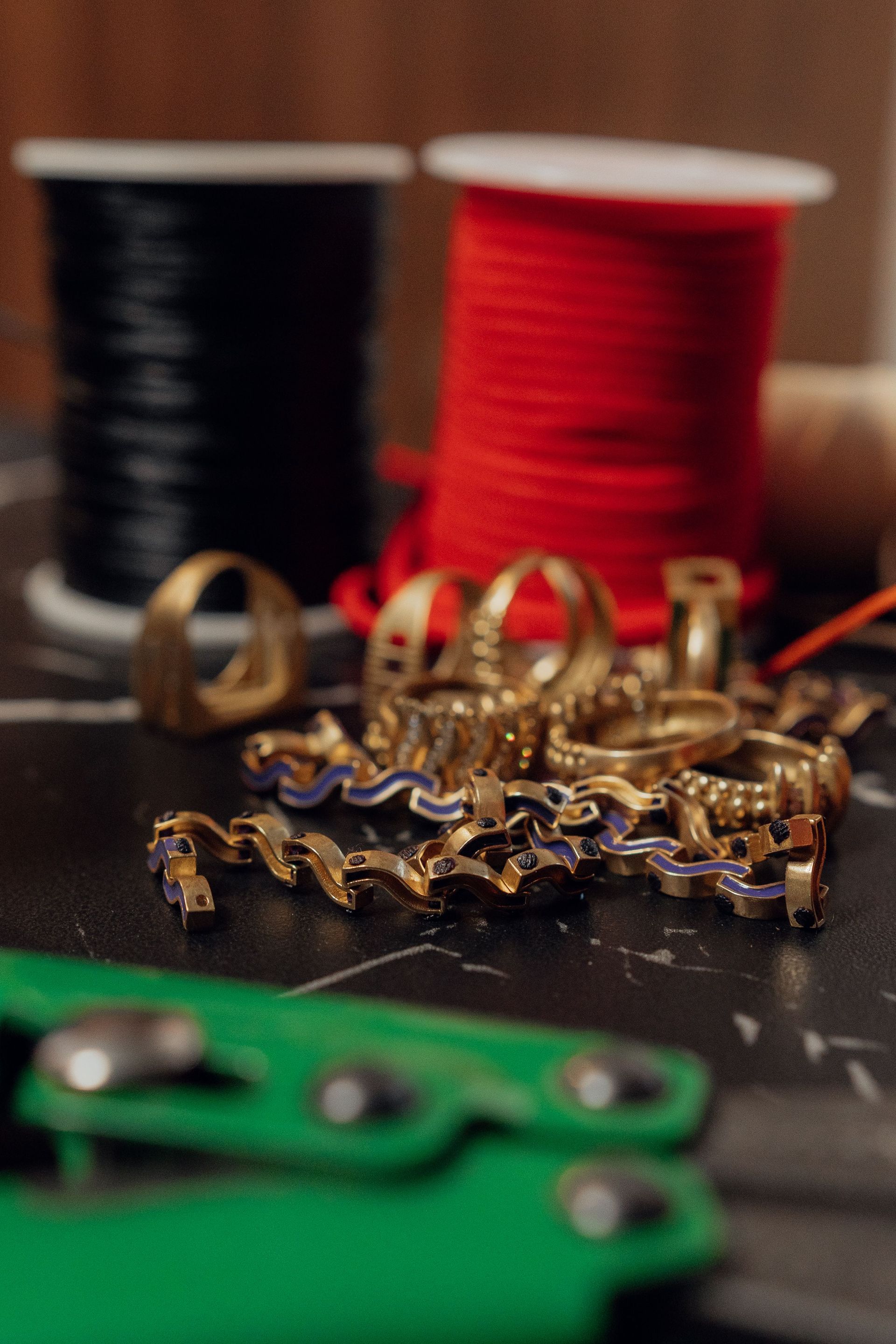 Gold jewelry on a table with black, red, and green thread spools in the background