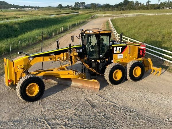 A yellow cat tractor is parked on the side of a dirt road.