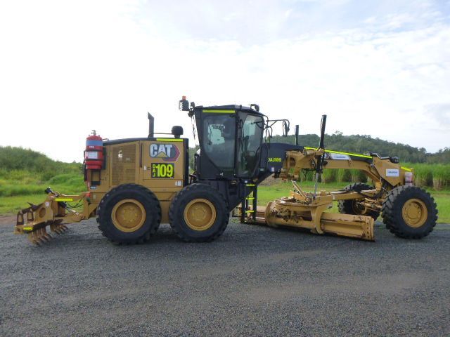 A yellow cat tractor is parked on the side of a dirt road.