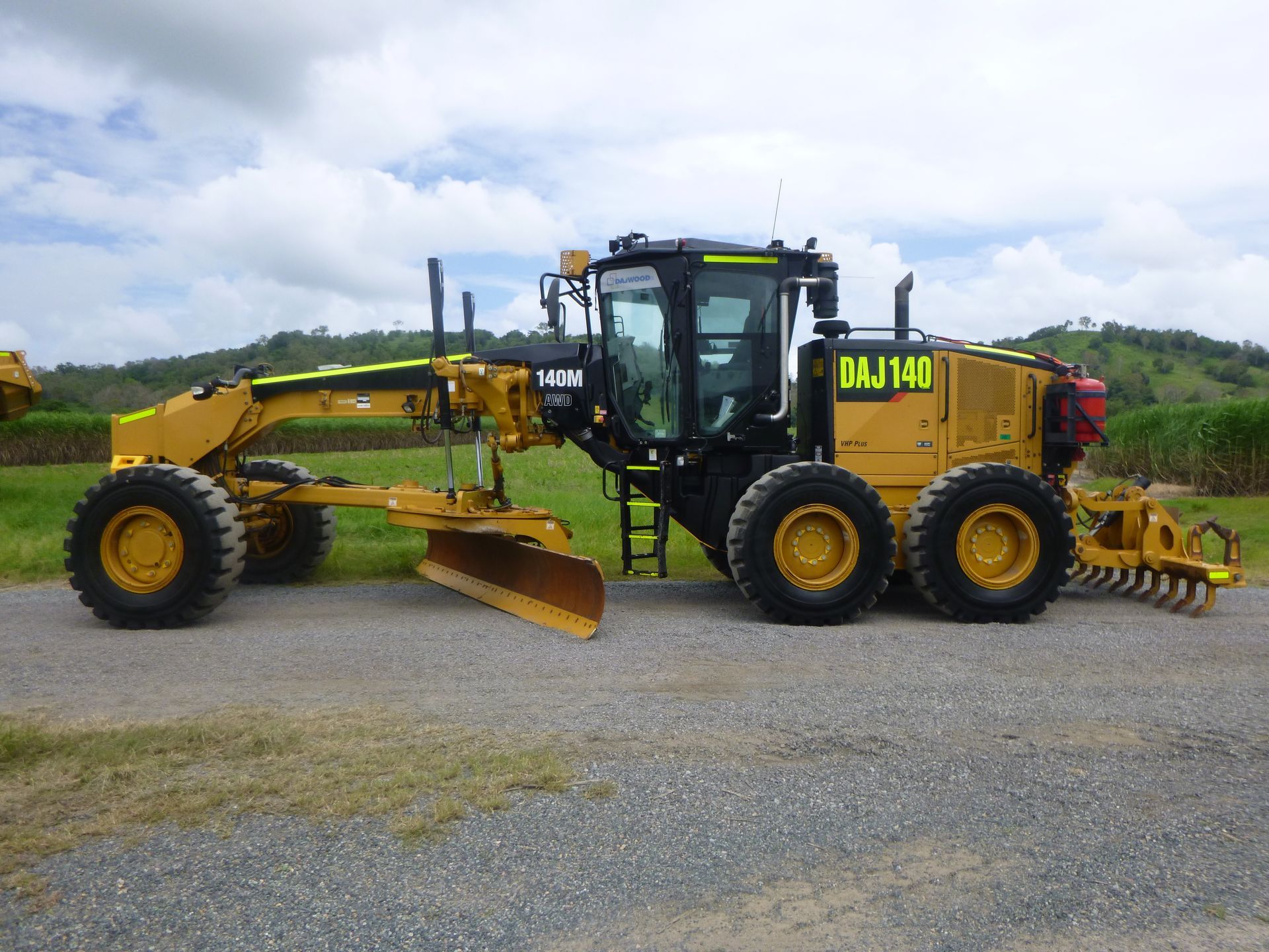A yellow cat tractor is parked on the side of a dirt road.