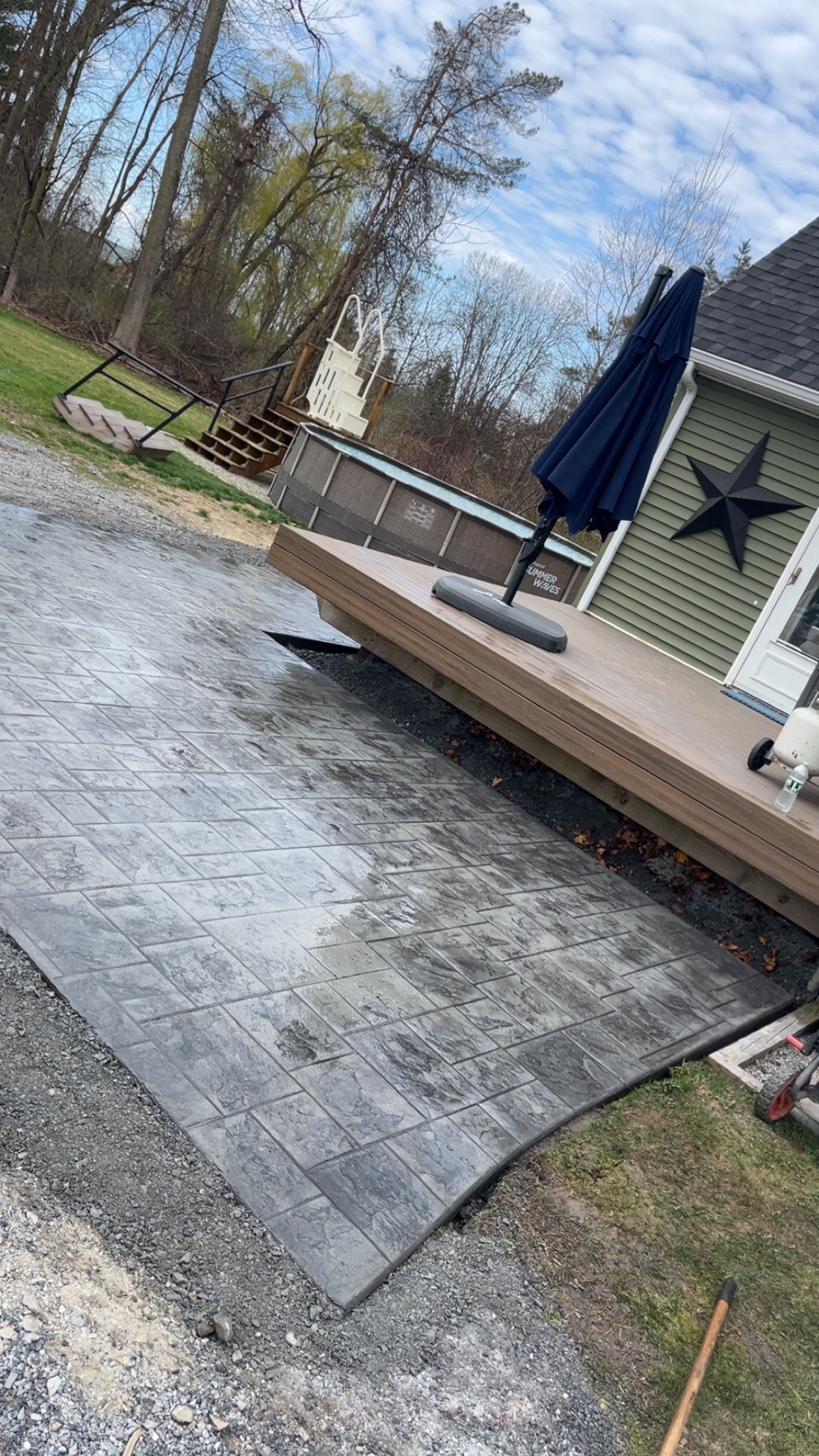Snow-dusted patio with a closed blue umbrella, white house siding, and trees in the background