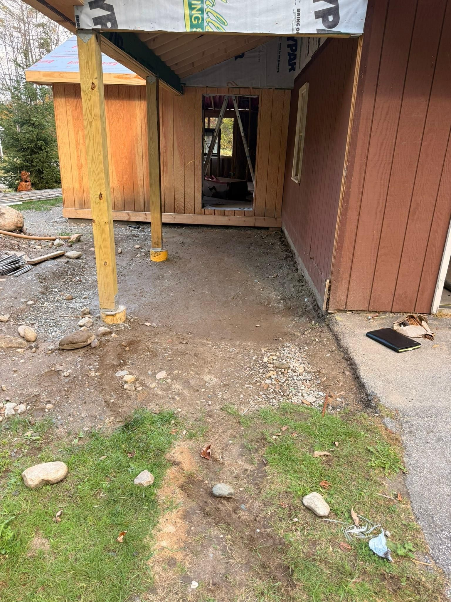 Rough dirt walkway beside a brown building with a covered entrance and yellow support posts
