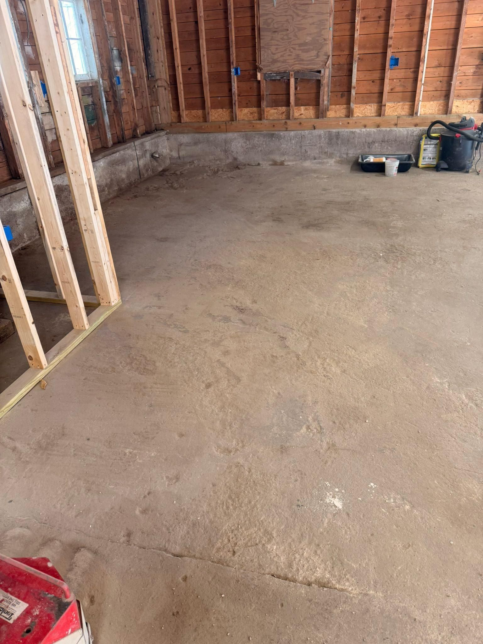 Unfinished room with exposed wooden studs and concrete floor, construction materials along the walls.