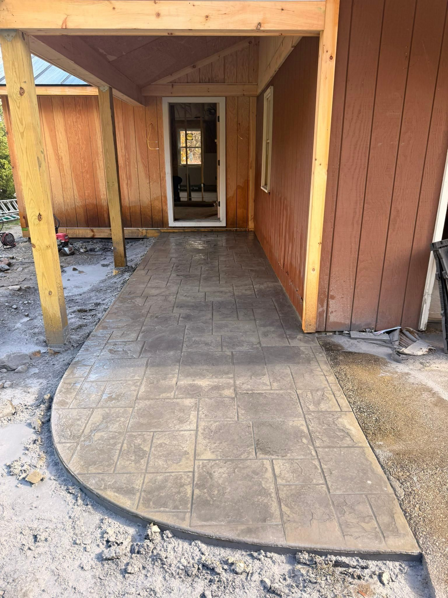 Covered wooden walkway with a concrete path and doorways at each end, seen during construction.