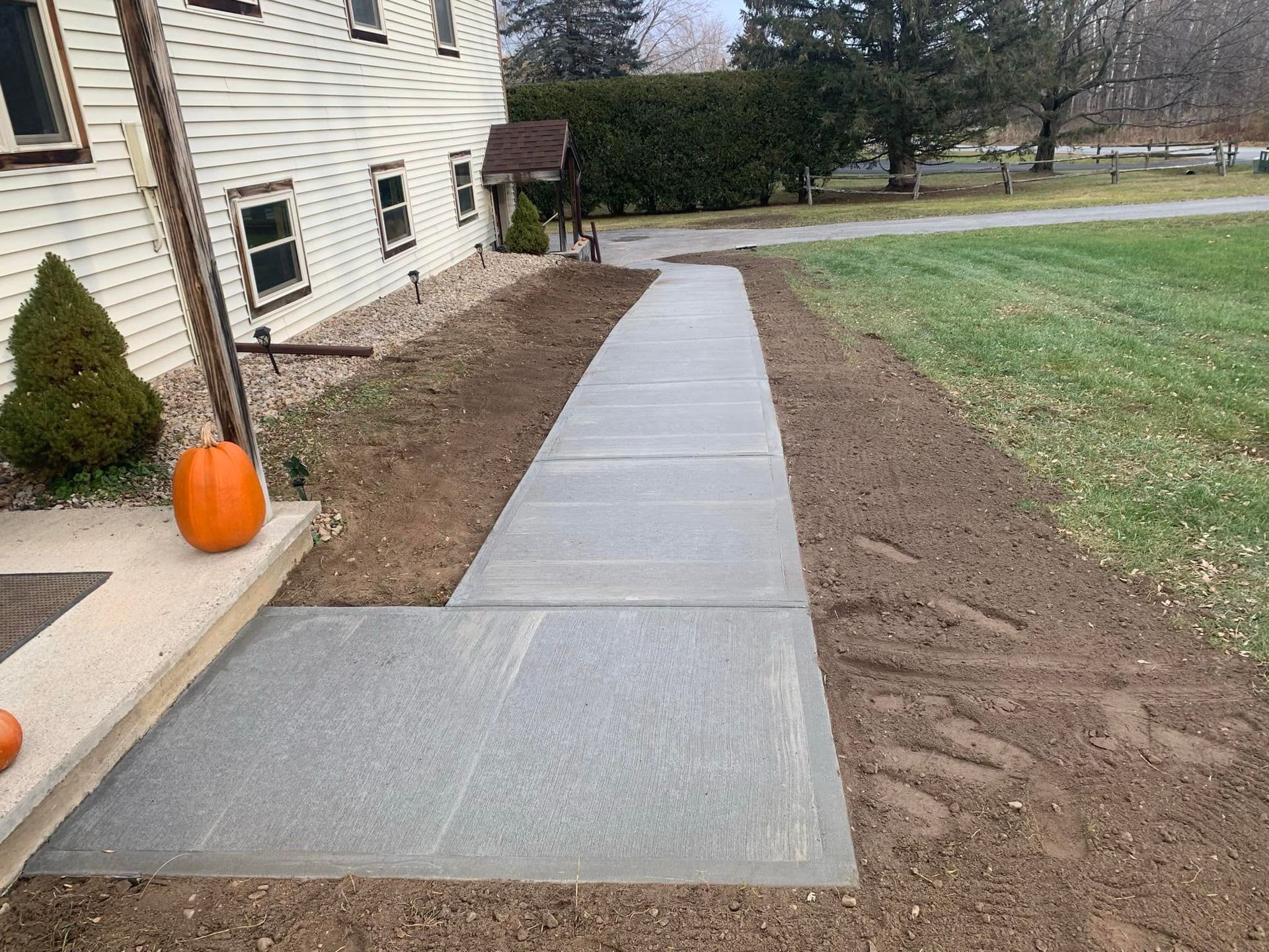 Concrete walkway beside house leading across yard, with pumpkins near the front steps