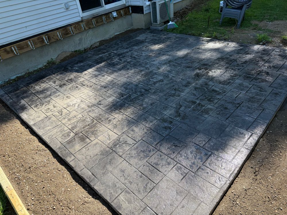 Freshly stamped concrete patio beside a house, with a grid pattern and partial shadow.