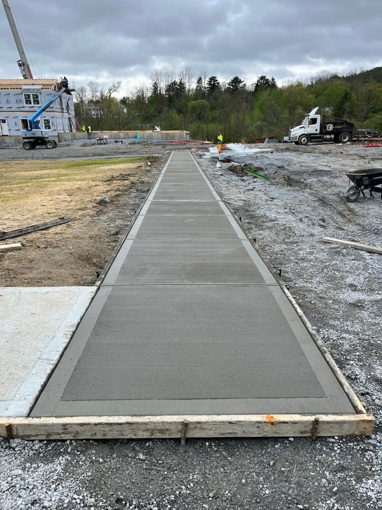 Long concrete walkway under construction leading toward a house and trees.