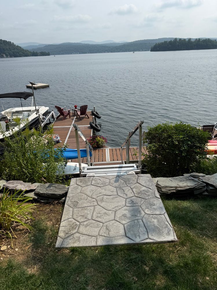 Dock leading to a lake with boats, people near the shore, and mountains in the distance.
