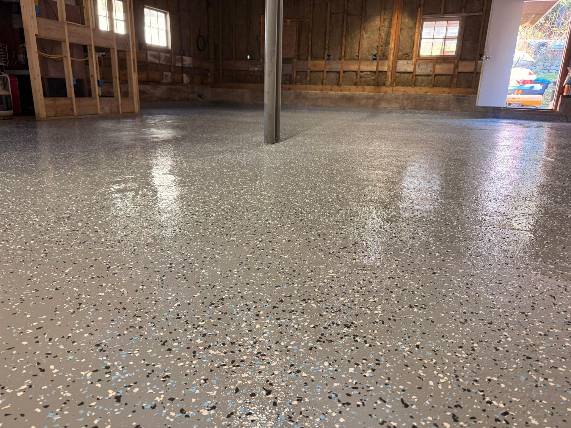 Empty room with speckled concrete floor, wooden walls, support post, and bright doorway light