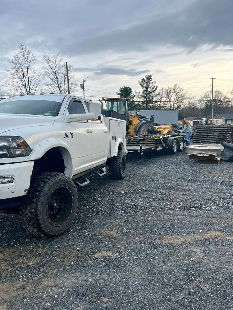 White pickup truck parked beside heavy equipment on a gravel lot at dusk