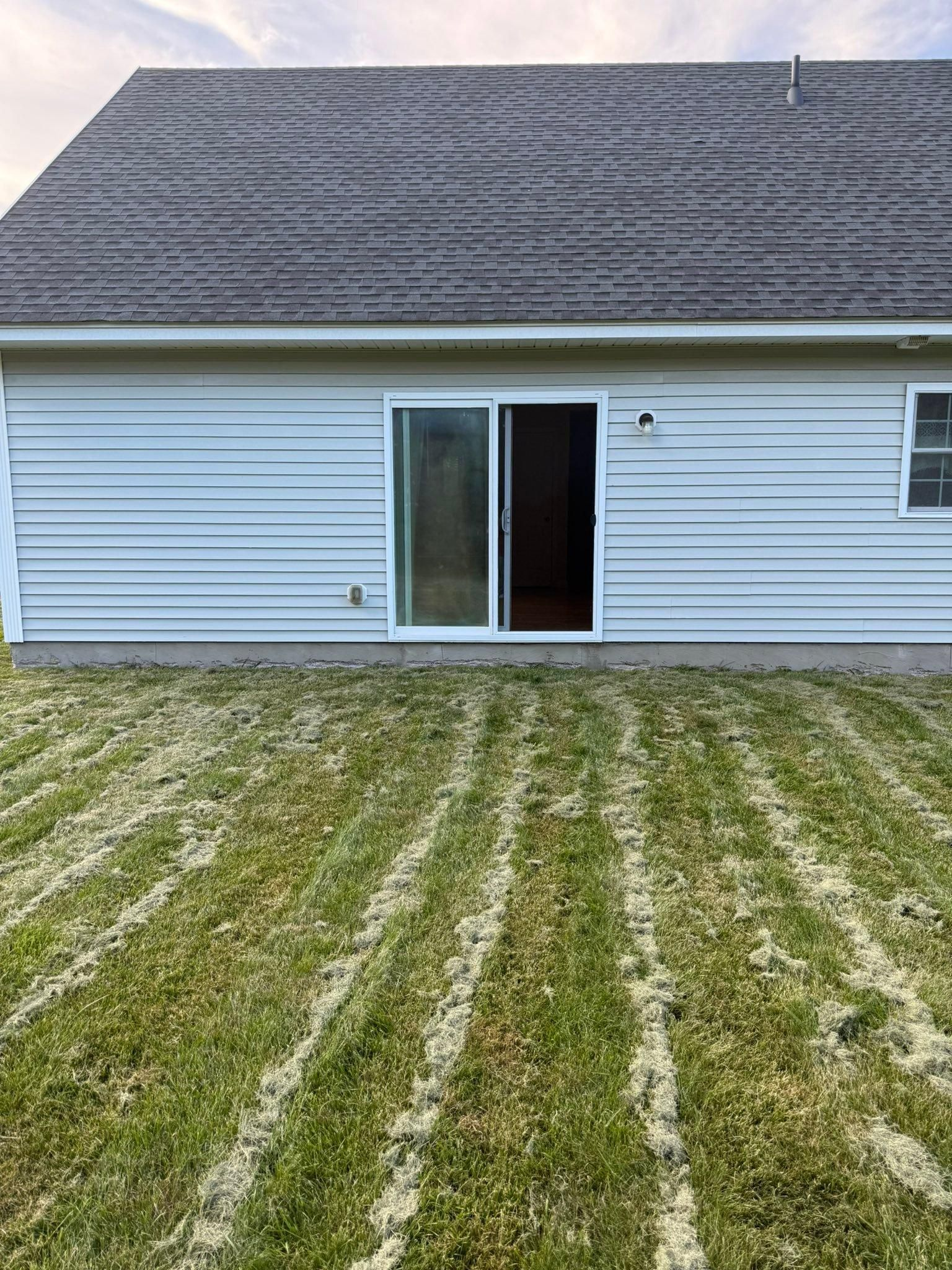 White house exterior with sliding glass door and patchy green lawn under a gray roof