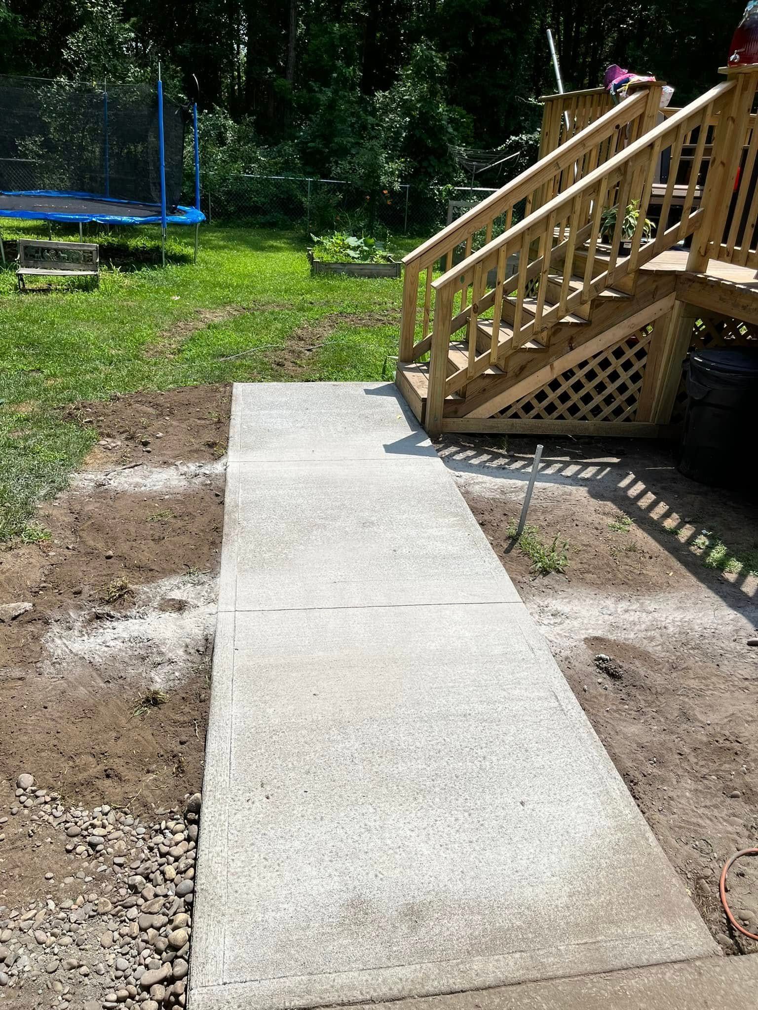 Concrete walkway beside wooden steps and a trampoline in a grassy yard