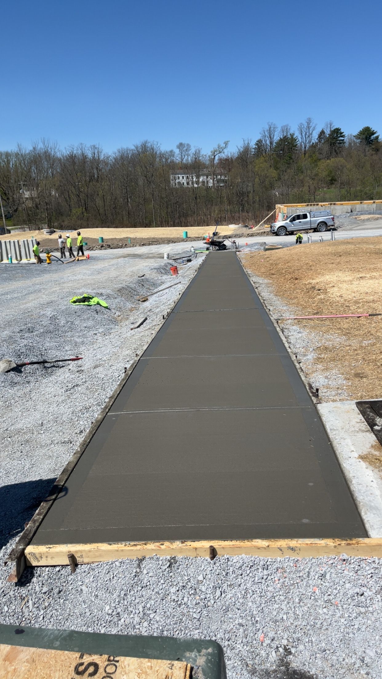 New concrete sidewalk under construction in a gravel lot under a clear sky