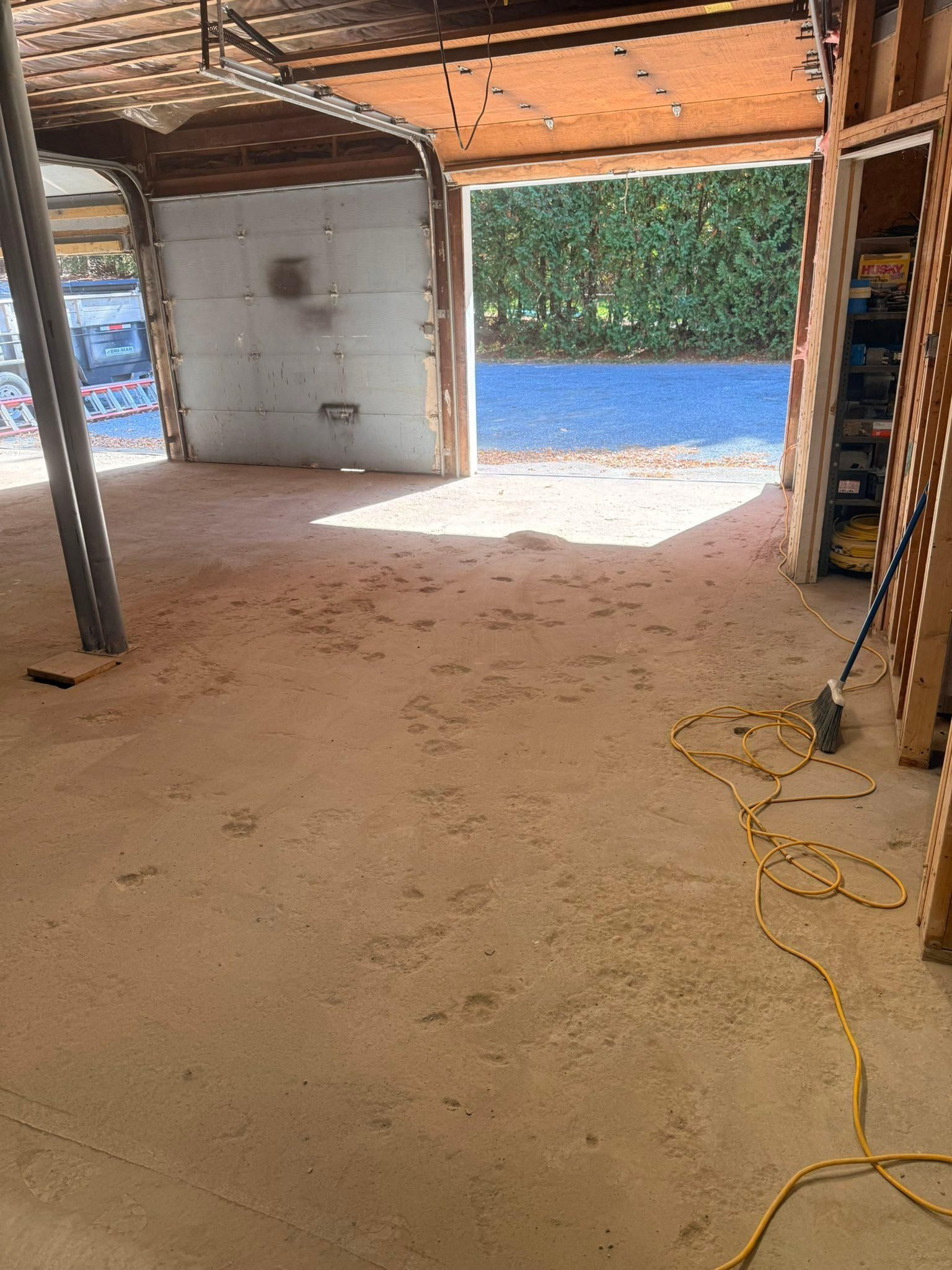 Empty garage with a concrete floor, open door, and a yellow extension cord on the ground.