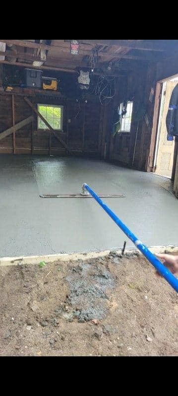 Indoor construction site with a newly poured gray concrete floor and a blue hose across the foreground