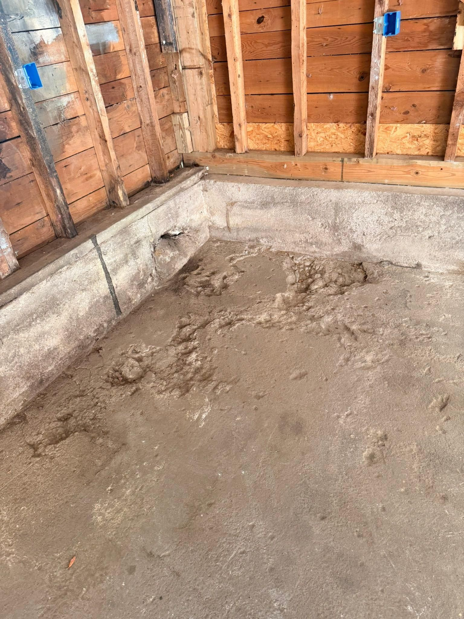 Bare concrete floor in an unfinished room with exposed wooden studs and a cinder block wall.