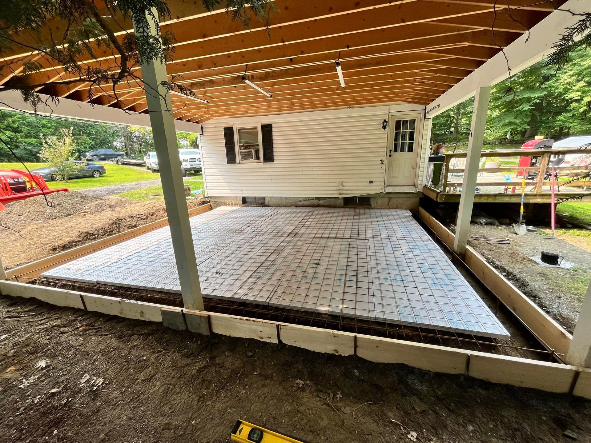 Covered patio with brick pavers under construction beside a small house, with exposed framing overhead.