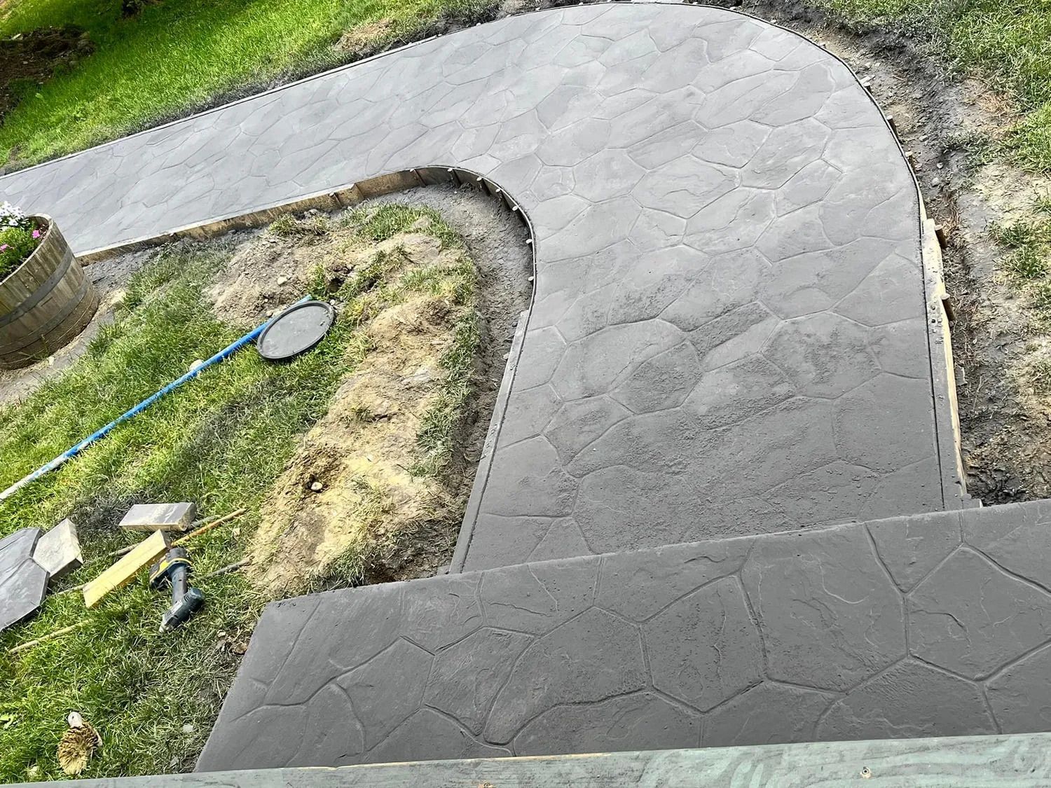 Freshly poured gray concrete path curving through a grassy yard, with tools nearby