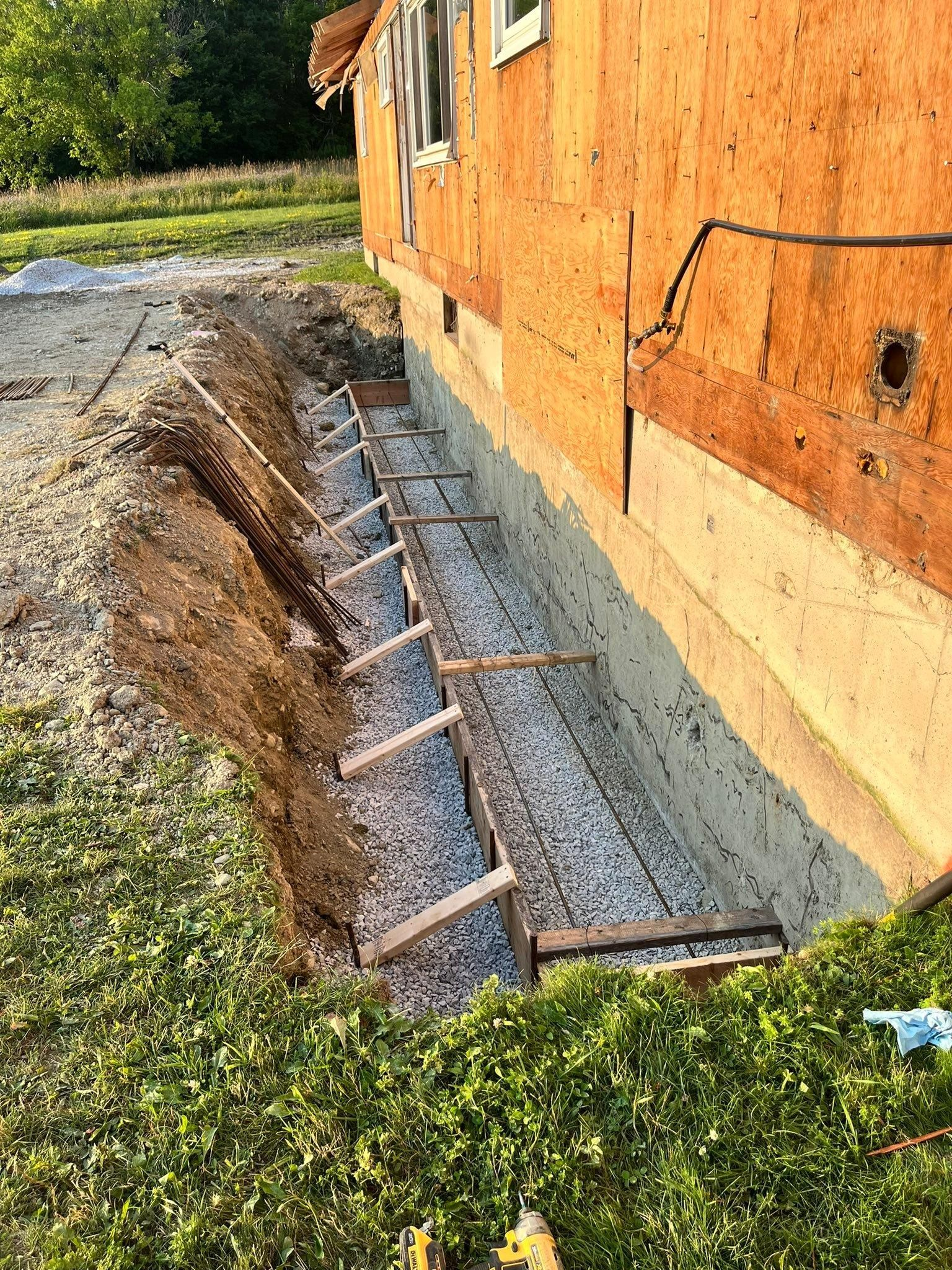 Temporary wooden shoring supports an excavated trench beside a brick building.