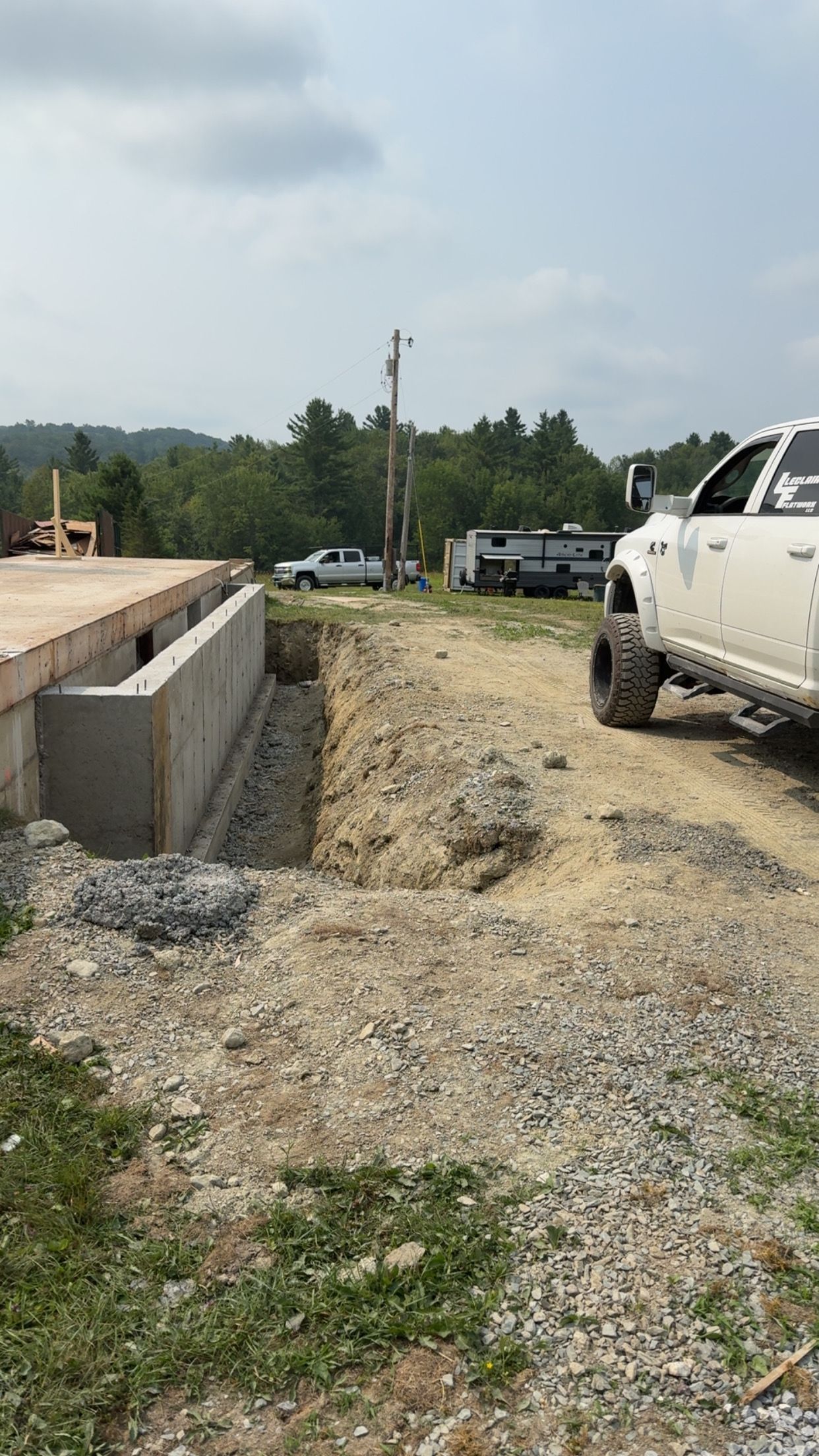 Construction site with excavated trench beside a concrete foundation and a white pickup truck.