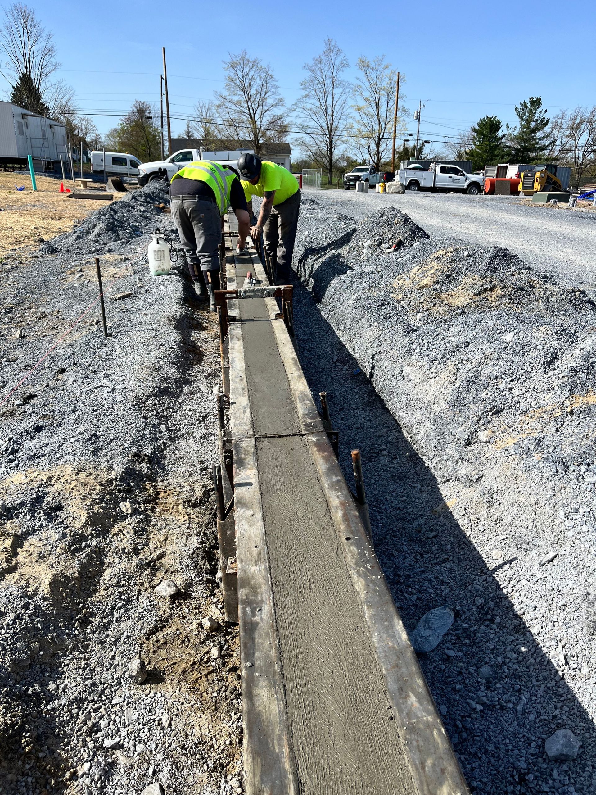 Workers in neon vests laying concrete curb on a gravel road construction site