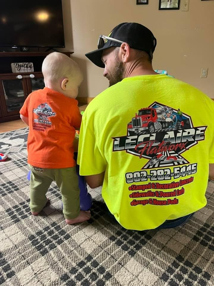 Man in neon yellow shirt and toddler in orange shirt sit on a plaid rug in a living room.