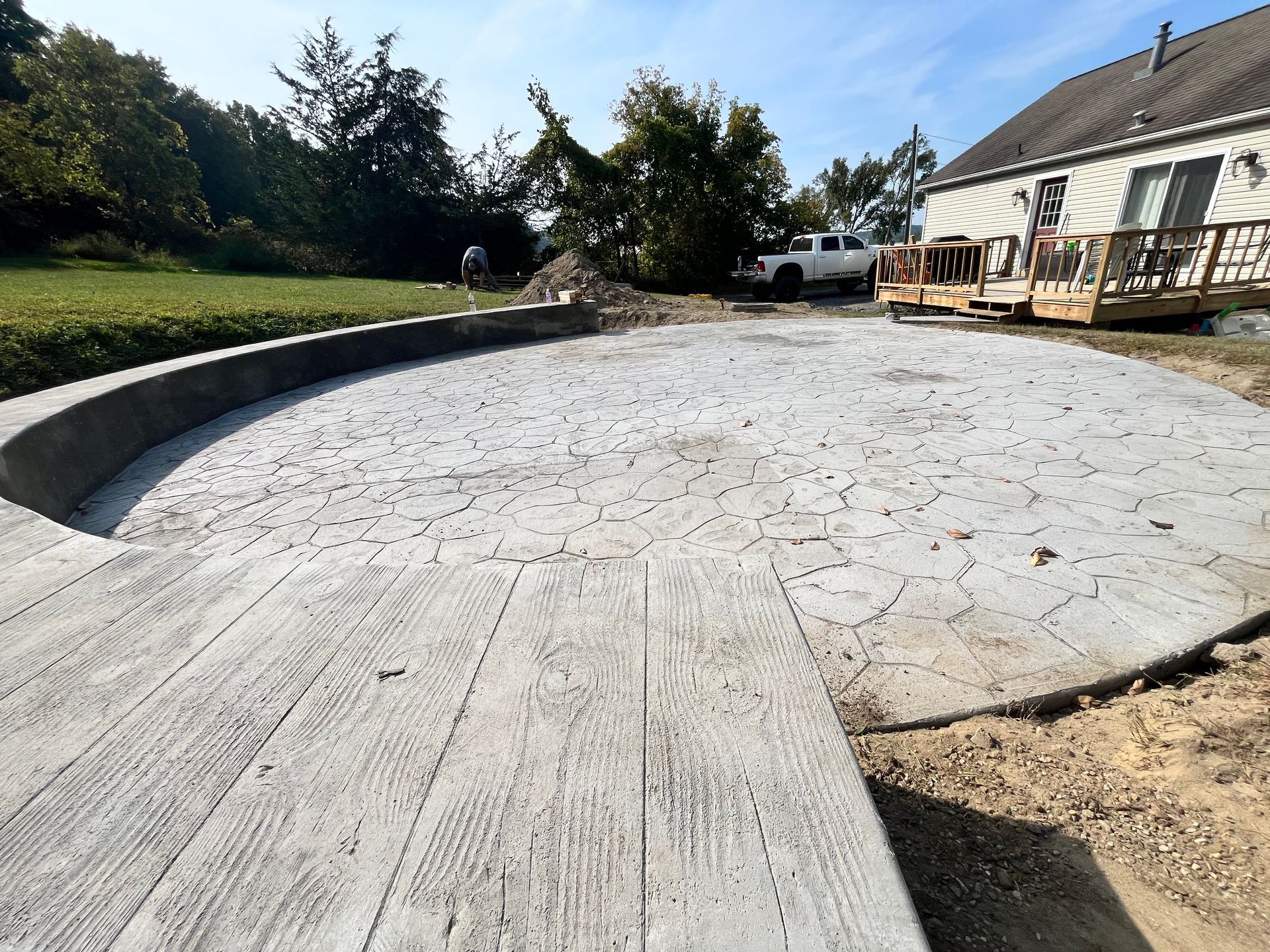 Curved concrete patio in a backyard beside a house, with trees and a wooden deck in the background