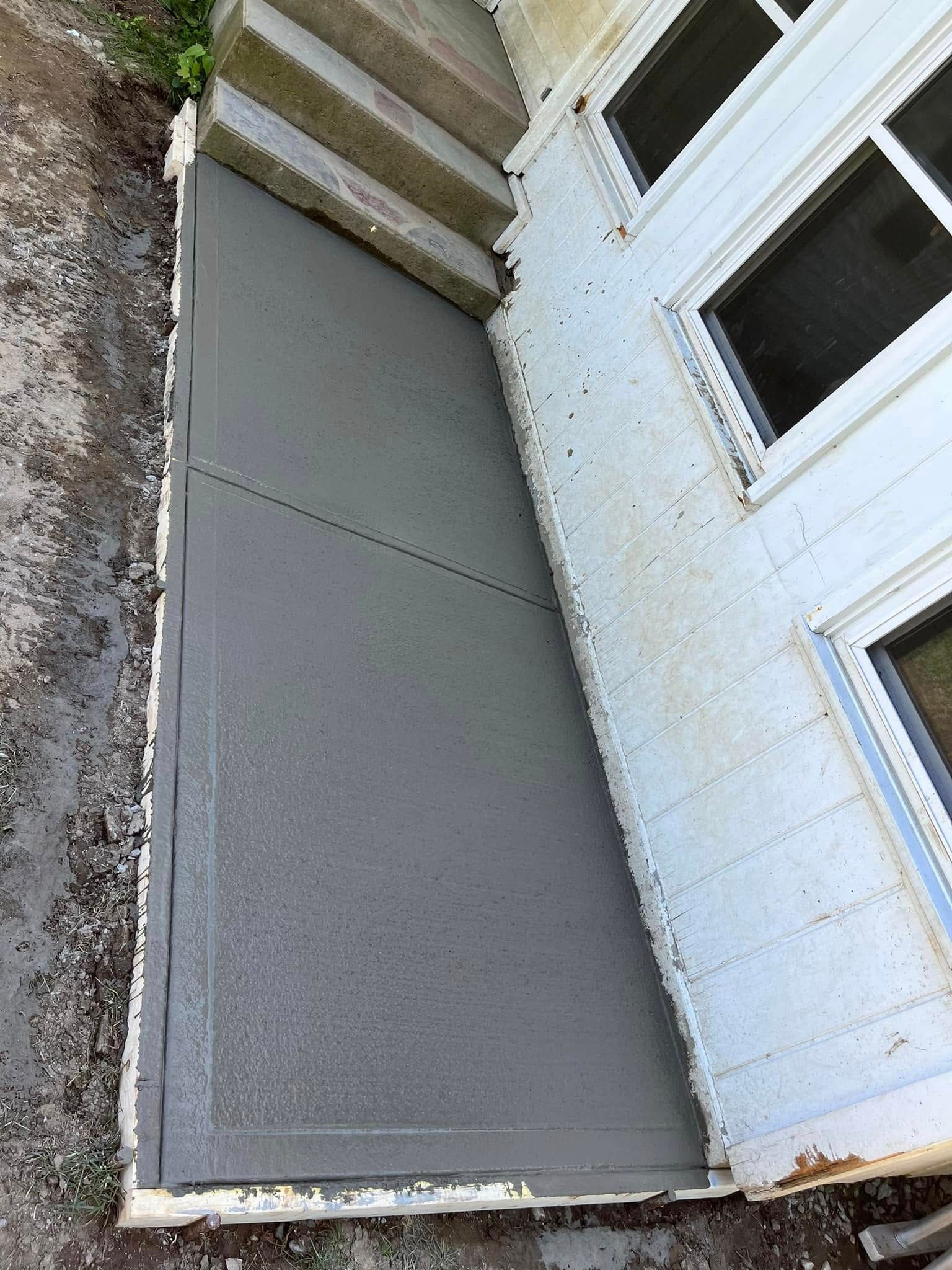 Gray basement window well beside a white brick house with basement windows and concrete steps