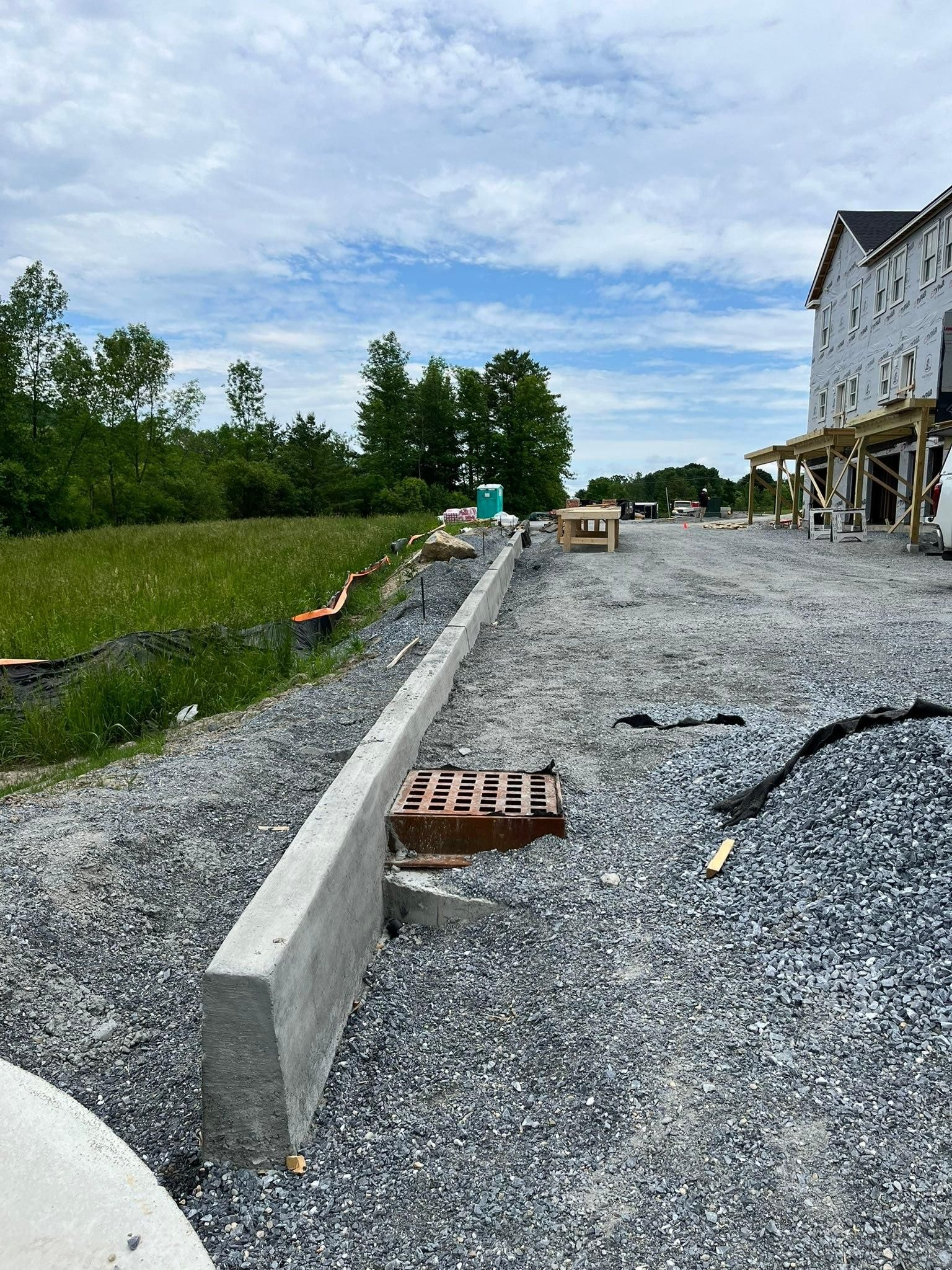 Gravel construction site beside a house, with a concrete retaining wall and stacked bricks under a cloudy sky