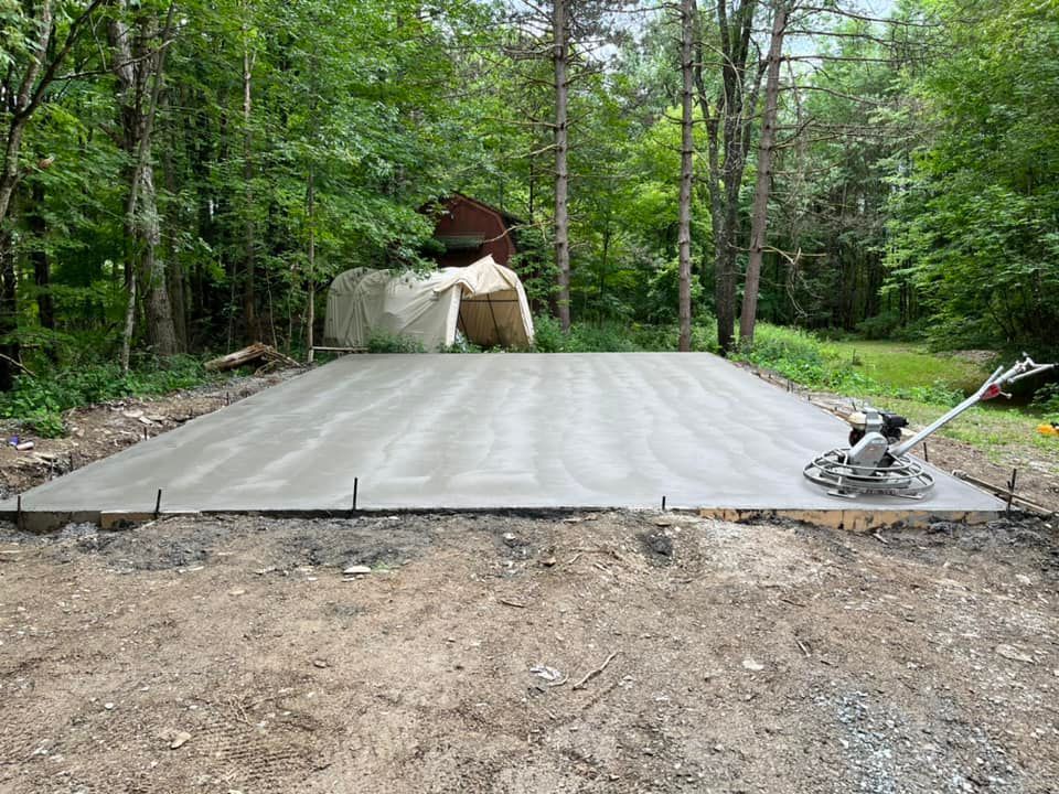 Fresh concrete slab in a wooded area, with a troweling machine on the right side.