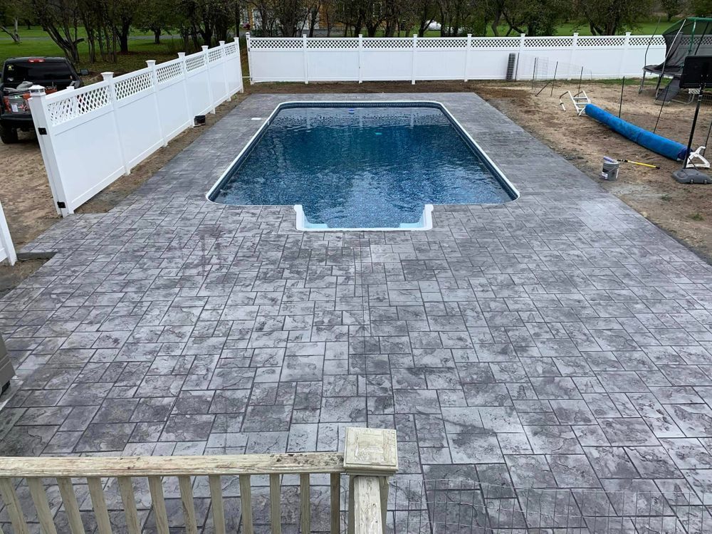 Backyard with a fenced in-ground pool and large stamped concrete patio.