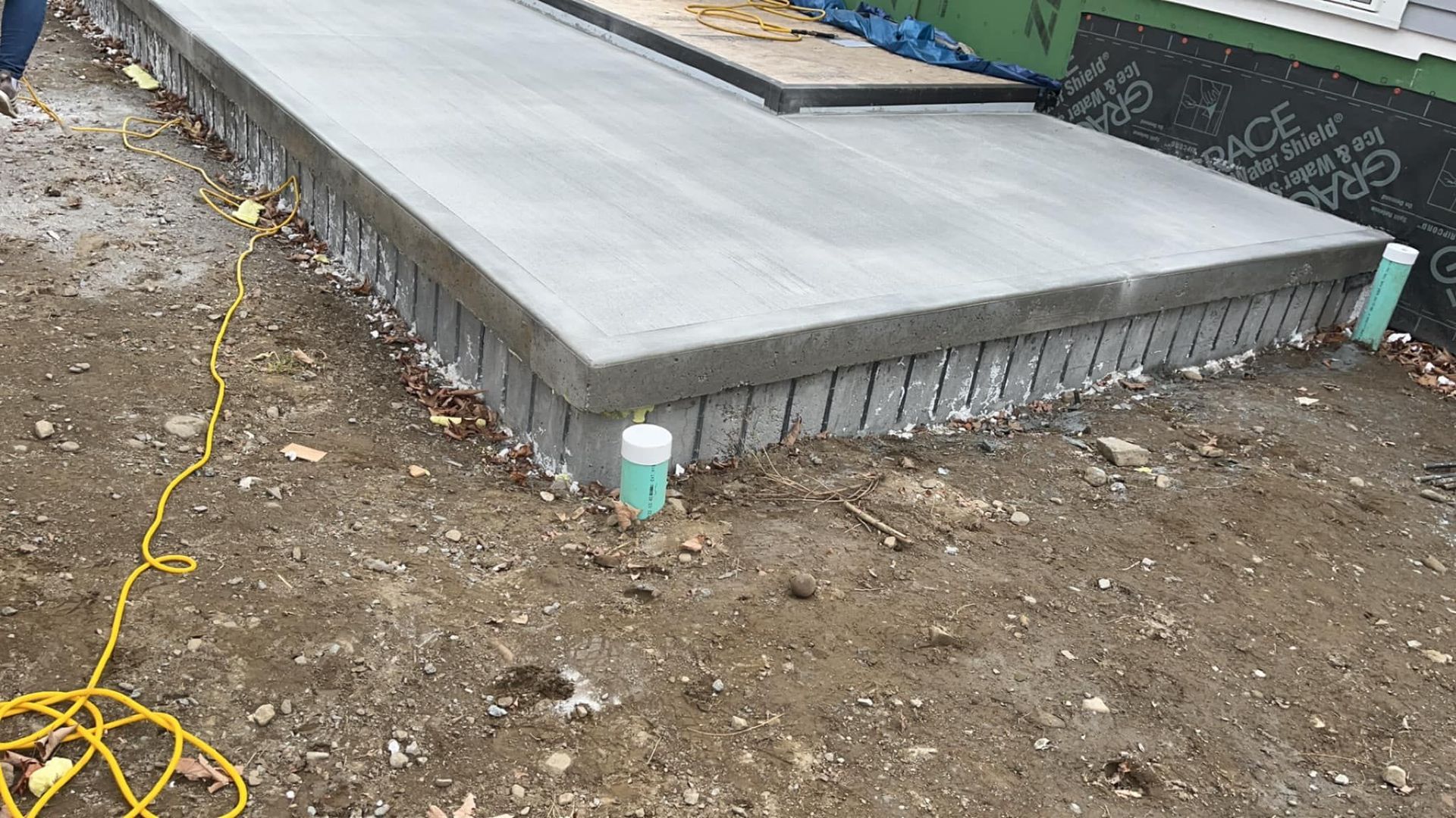 Fresh concrete slab foundation on a dirt lot, with rebar edge and a cord nearby