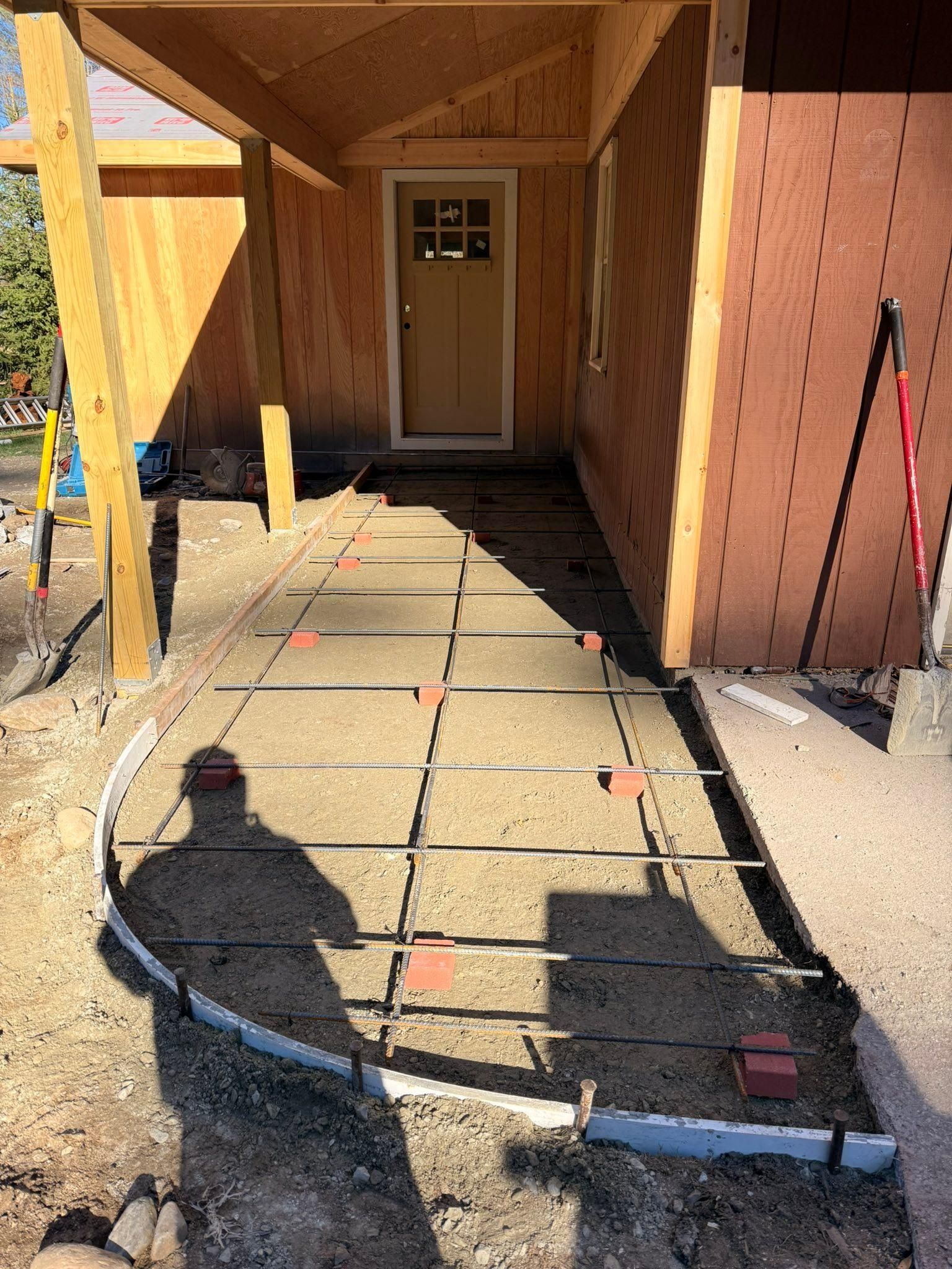 Unfinished front walkway with pavers, exposed wiring, and a door under a wooden overhang at a house entrance