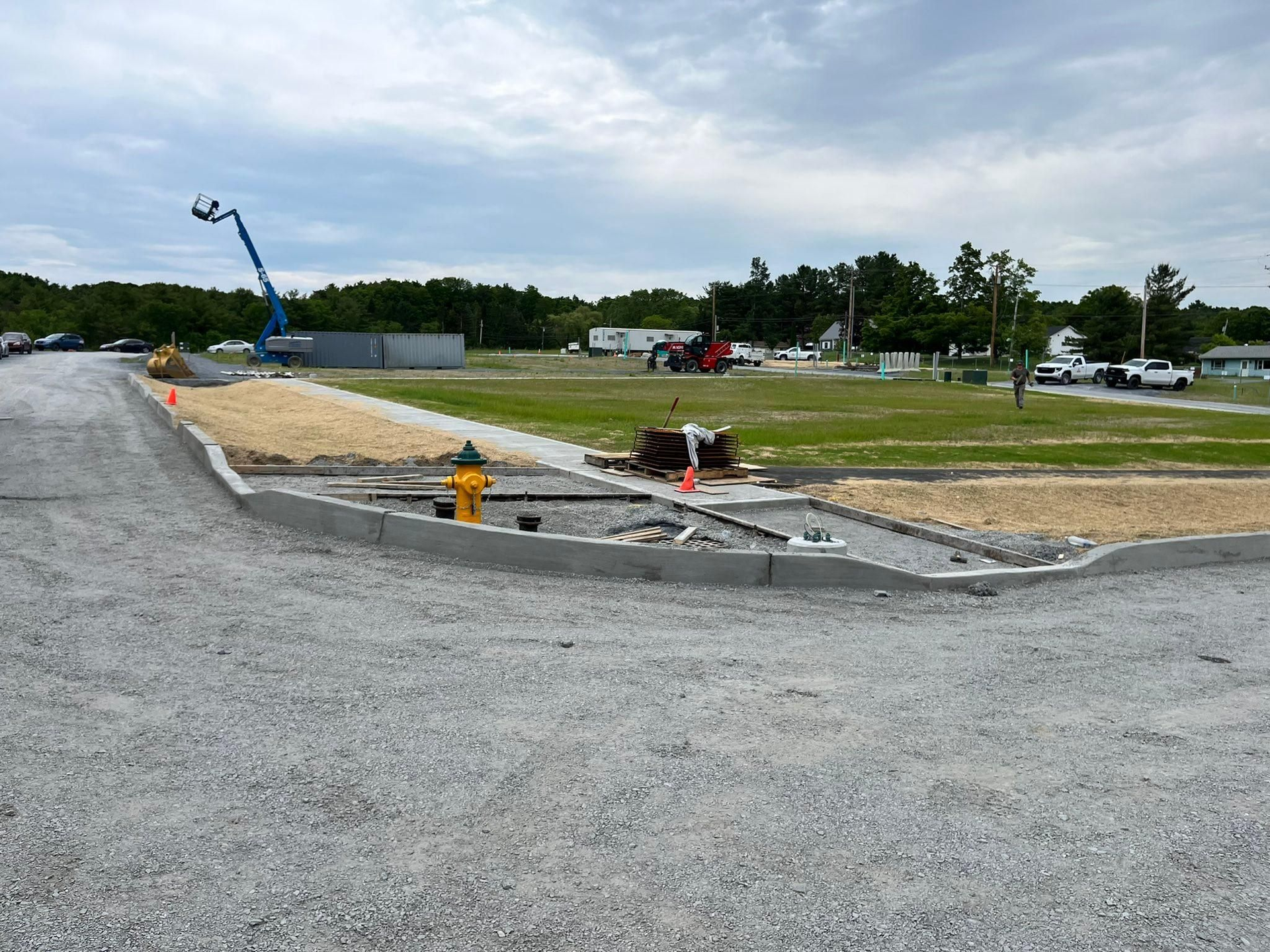 Construction site with gravel road, curb edging, yellow fire hydrant, and a blue crane in the distance