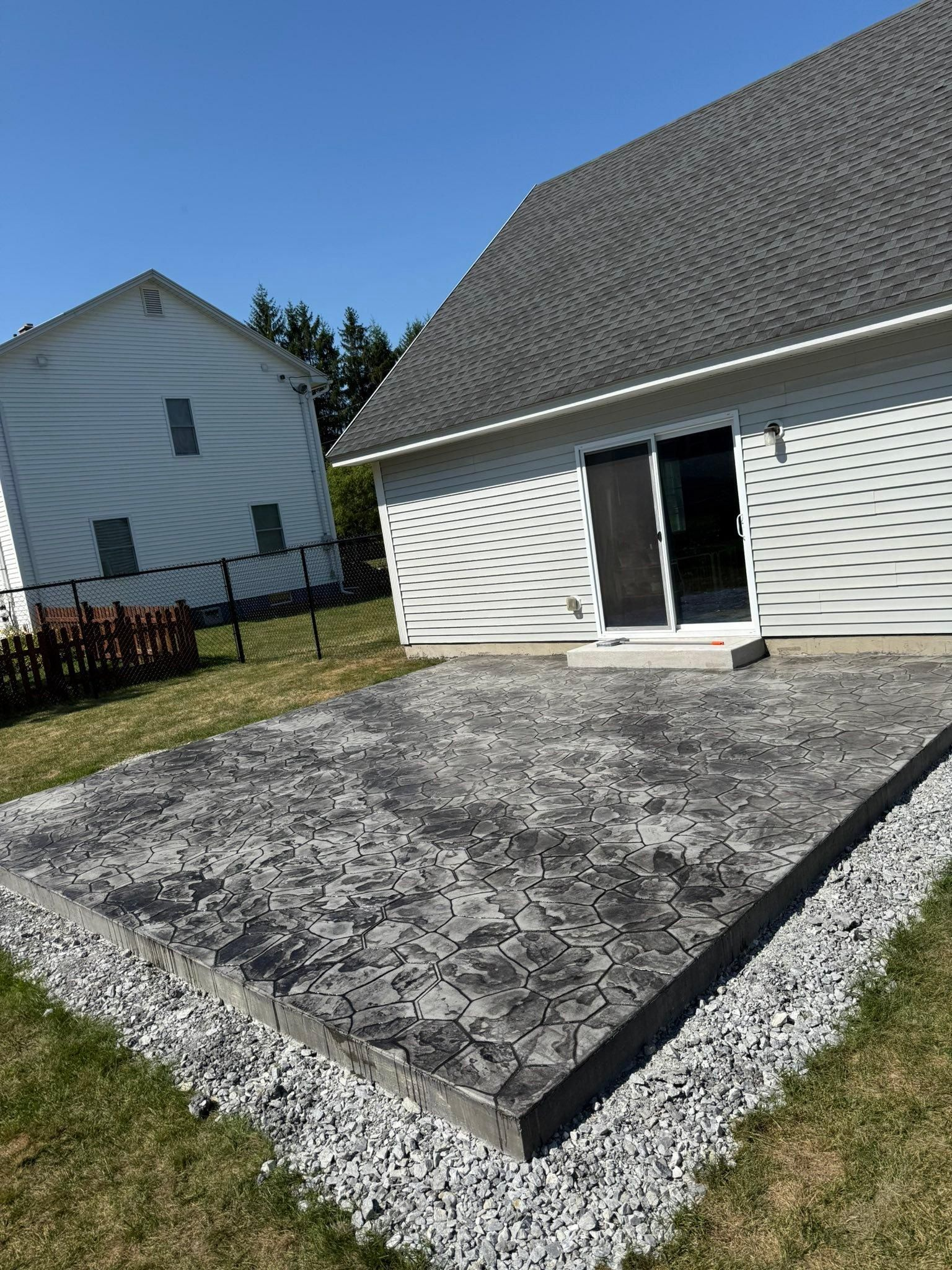 Backyard concrete patio beside a white house with sliding glass doors and gravel edging
