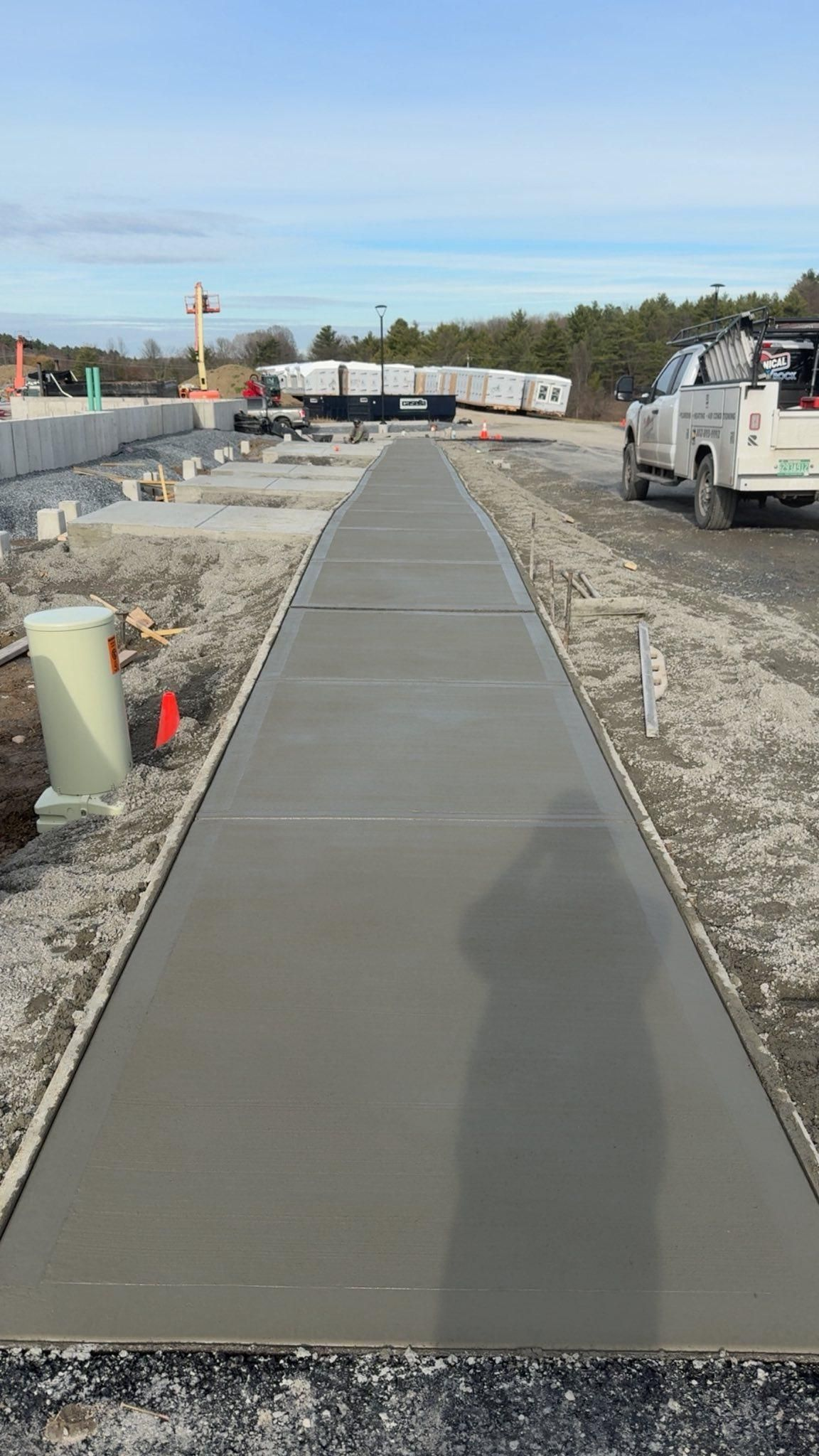Concrete sidewalk under construction beside gravel and parked trucks on a sunny day